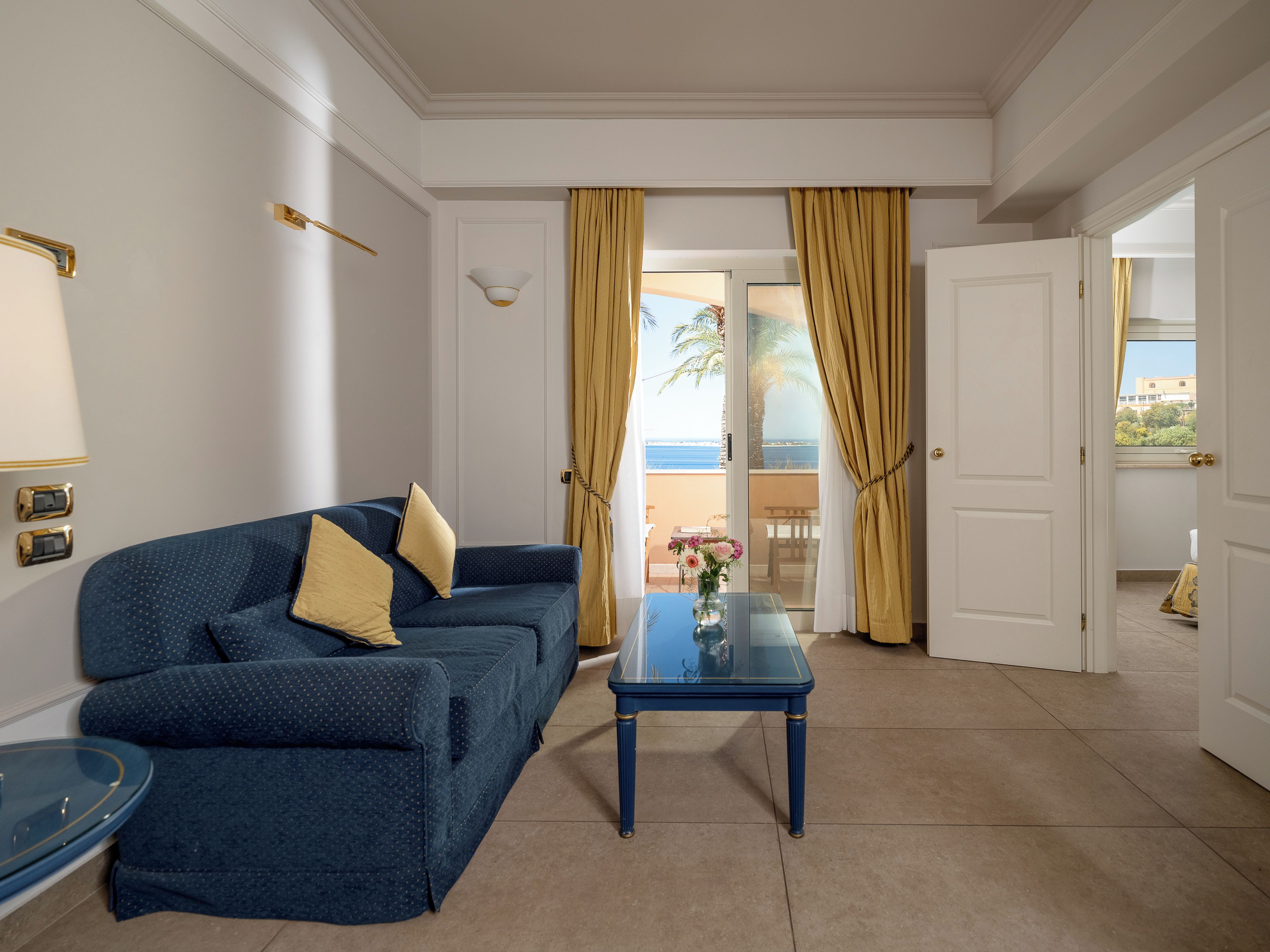 A room with a blue sofa, a glass coffee table, and a view of the sea through a door.