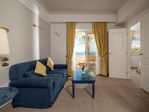 A room with a blue sofa, a glass coffee table, and a view of the sea through a door. - Altafiumara Resort & Spa (Villa San Giovanni)
