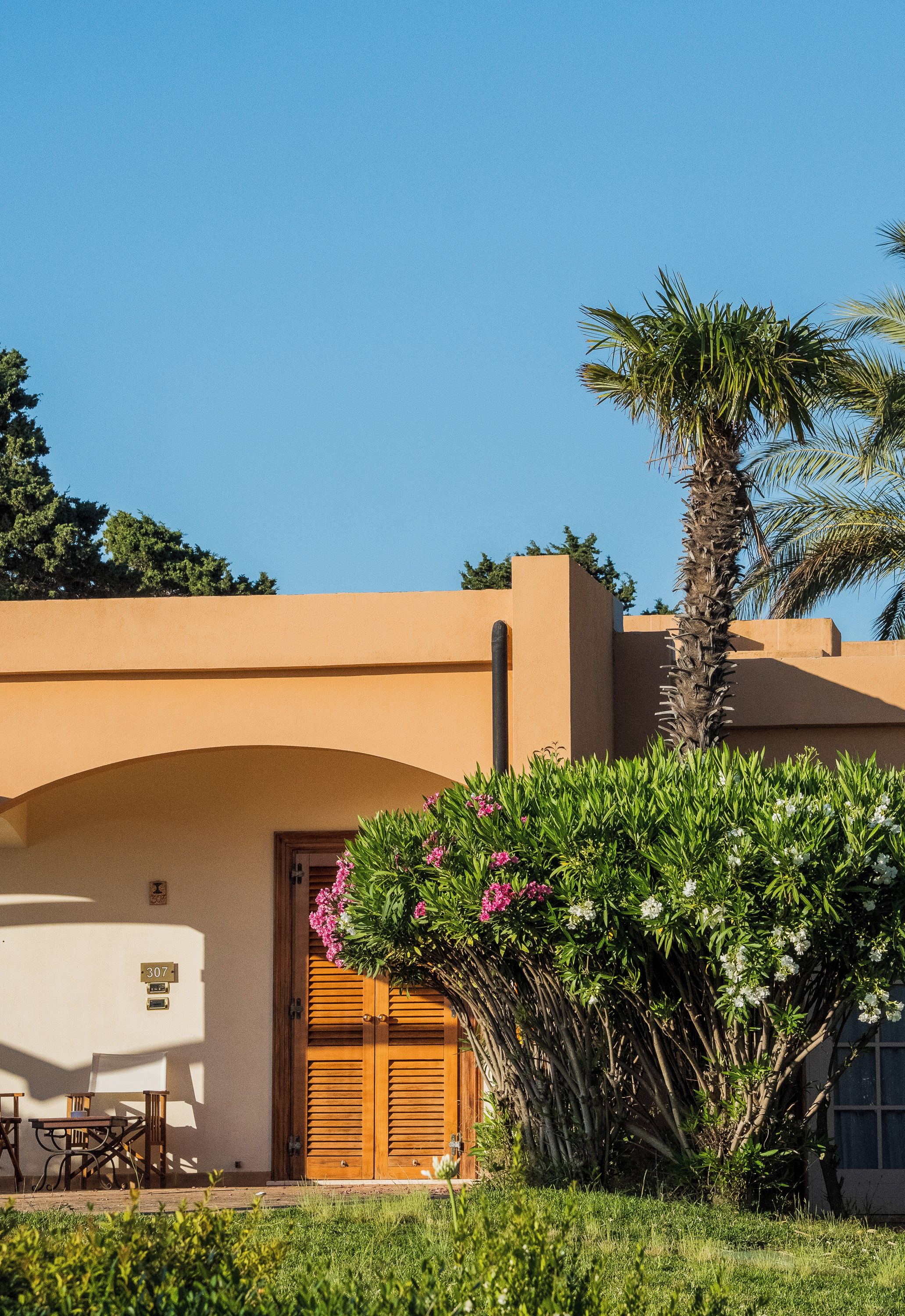 Un edificio con facciata beige, una porta in legno e un piccolo patio con tavolo e sedie.
