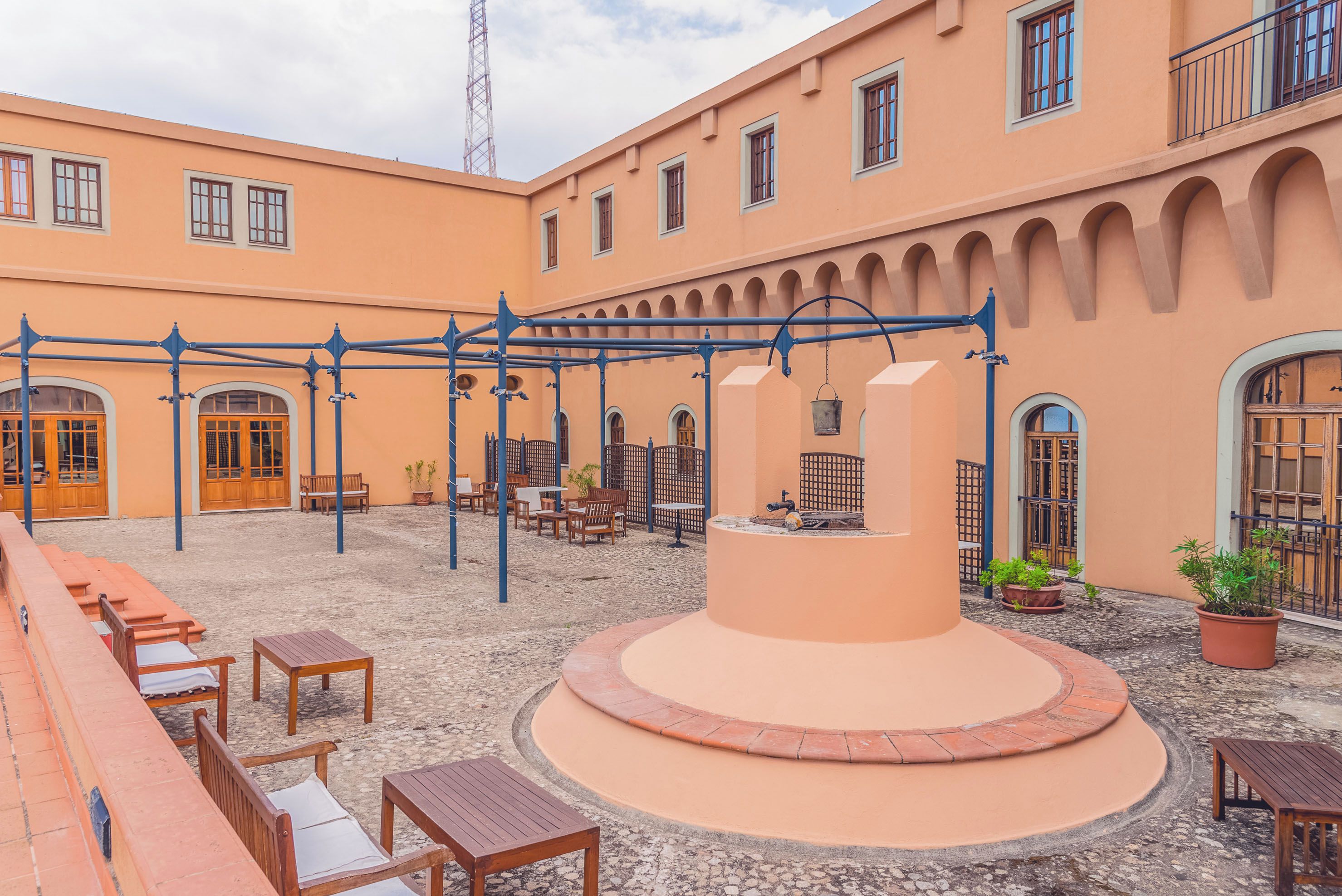 A courtyard with outdoor seating, a central fountain, and a building with arches and windows.