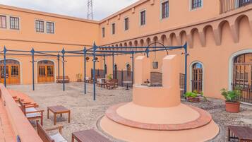 A courtyard with outdoor seating, a central fountain, and a building with arches and windows.