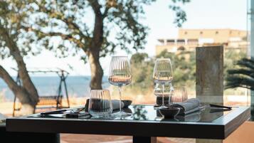 Una mesa dispuesta con copas de vino, un bol y cubiertos, con vistas a un paisaje con árboles y un edificio al fondo.