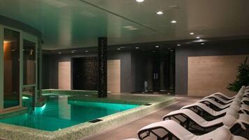 A modern indoor pool area with a clear pool, lounge chairs, and a spa-like ambiance.