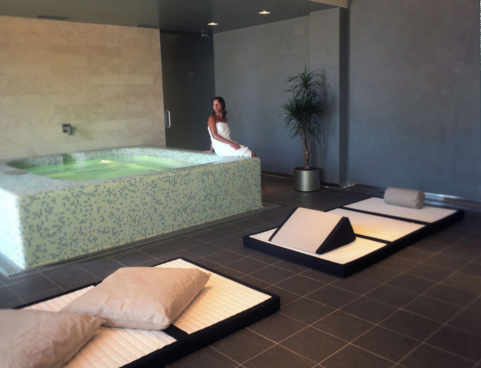 Una stanza spa con vasca idromassaggio, lettini per massaggi e una pianta in vaso.