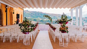 A wedding ceremony setup with white chairs and floral centerpieces, a white aisle, and a scenic view of hills in the background. - Altafiumara Resort & Spa (Villa San Giovanni)