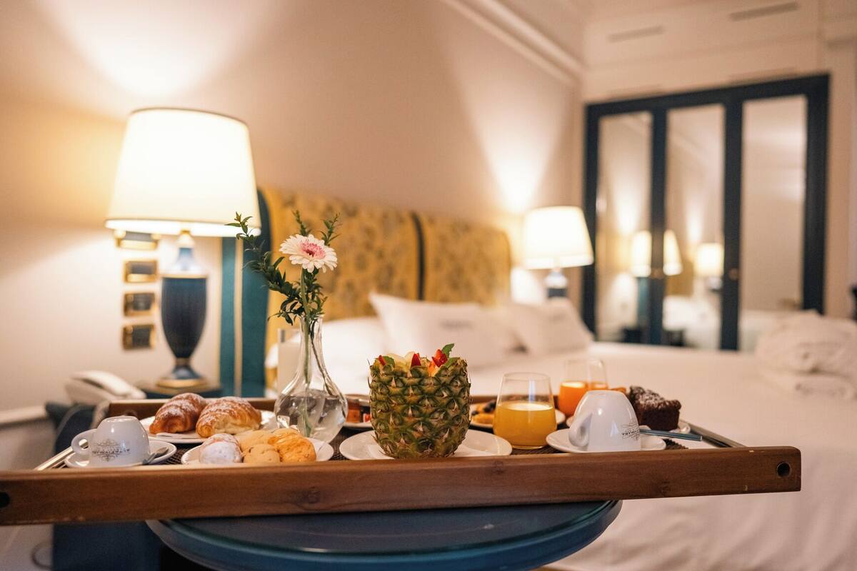 A hotel room with a breakfast tray on a table, including croissants, a pineapple, and orange juice.