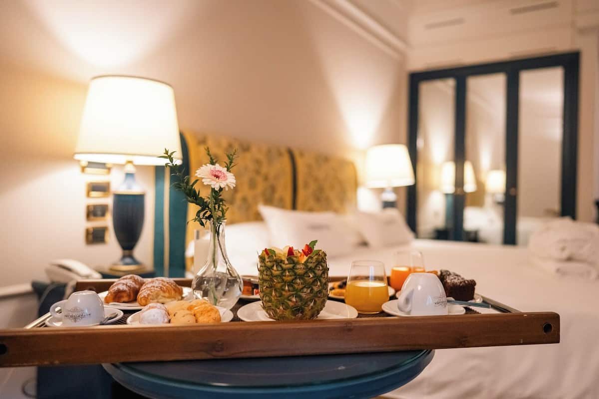 Ett hotellrum med ett frukostbricka på ett bord, innehållande croissanter, en ananas och apelsinjuice.
