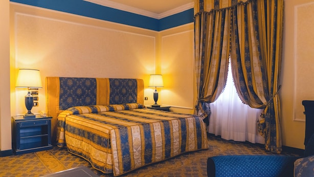 Une chambre d’hôtel avec un grand lit, deux tables de chevet avec des lampes, une chaise et une fenêtre avec des rideaux.