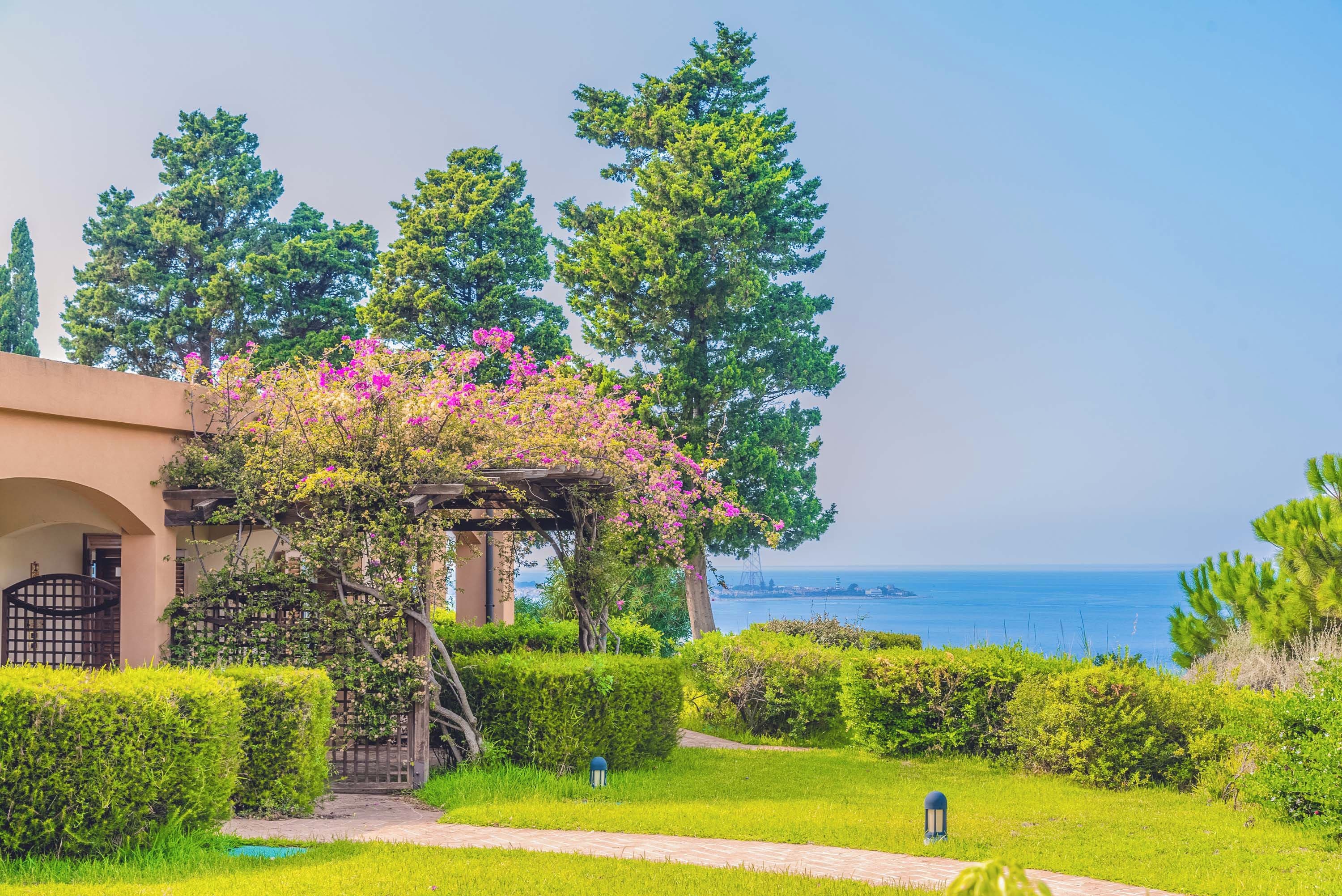 A landscaped garden with a pergola, a pathway, and a view of the sea.