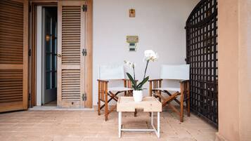 A wooden door with a sliding mechanism, a small table with a white vase and two white orchids, and two wooden chairs with white cushions.