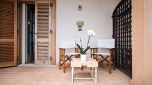 A wooden door with a sliding mechanism, a small table with a white vase and two white orchids, and two wooden chairs with white cushions. - Altafiumara Resort & Spa (Villa San Giovanni)