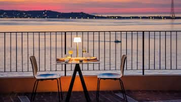 Un tavolo con due sedie, una lampada e un menu su un balcone con vista su un corpo d'acqua al tramonto.