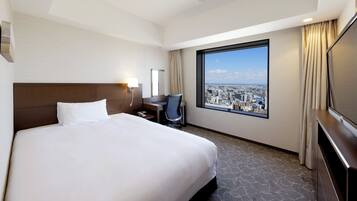 Habitación de hotel con una cama grande, un escritorio con silla, televisor y ventana con vista a la ciudad.