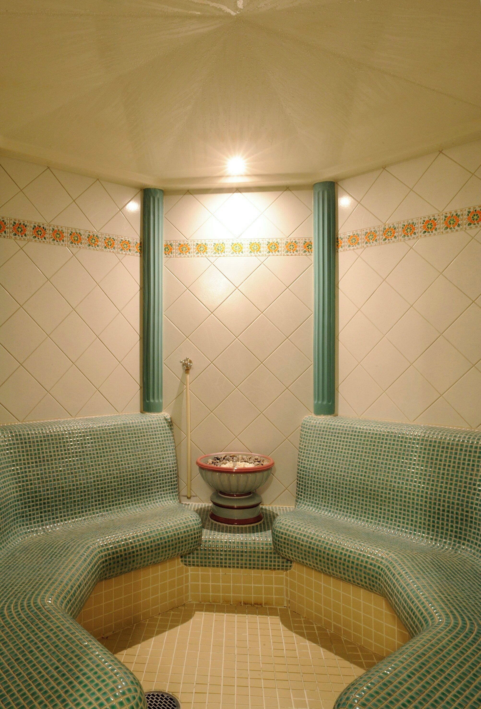 Une salle de bain avec un sol carrelé, un lavabo et deux coins salon agrémentés de coussins verts.