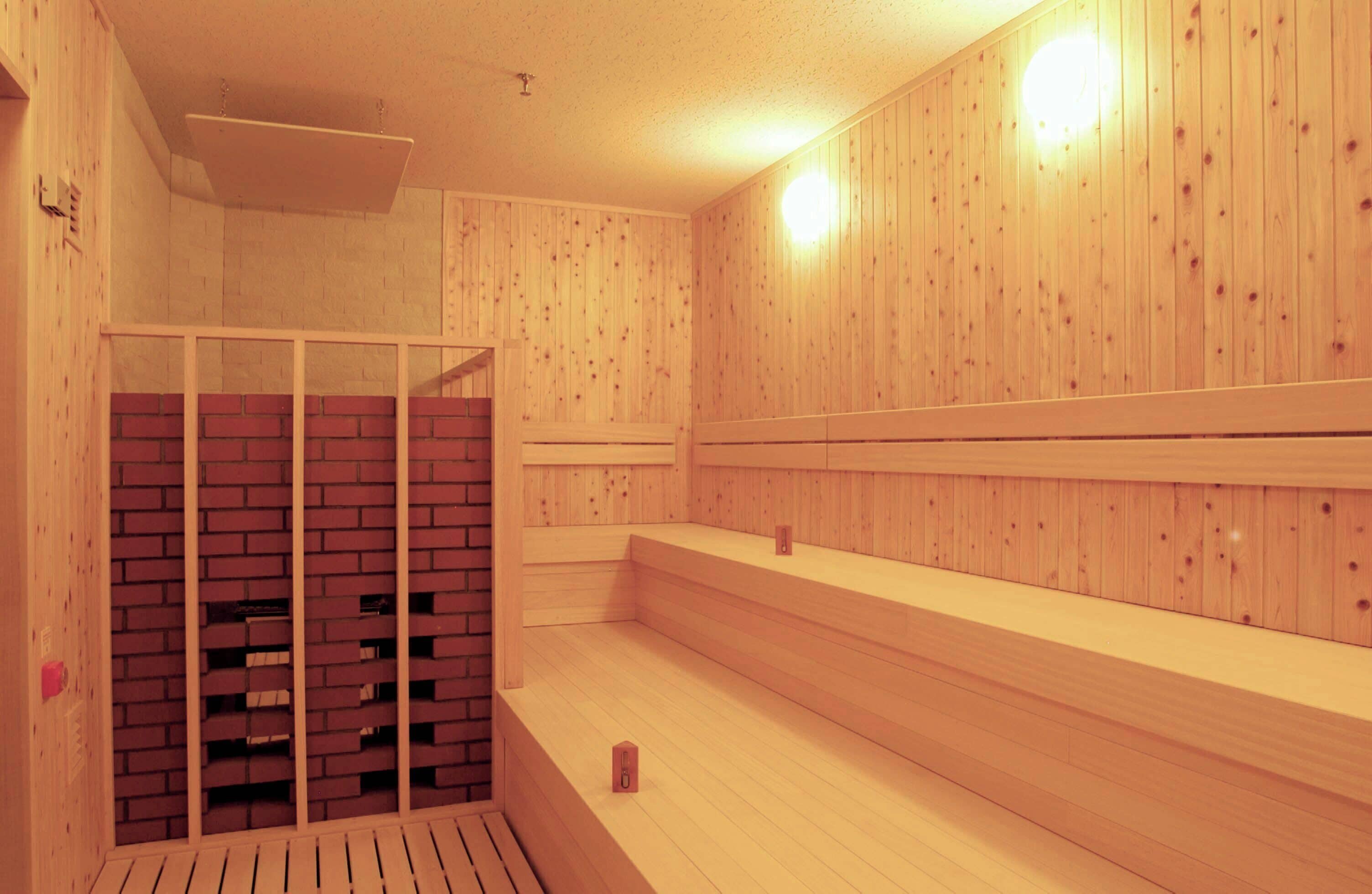 A sauna with wooden walls and benches, a brick wall section, and a ceiling light.