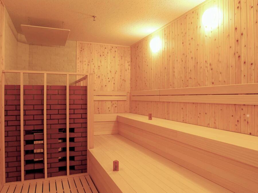 A sauna with wooden walls and benches, a brick wall section, and a ceiling light.