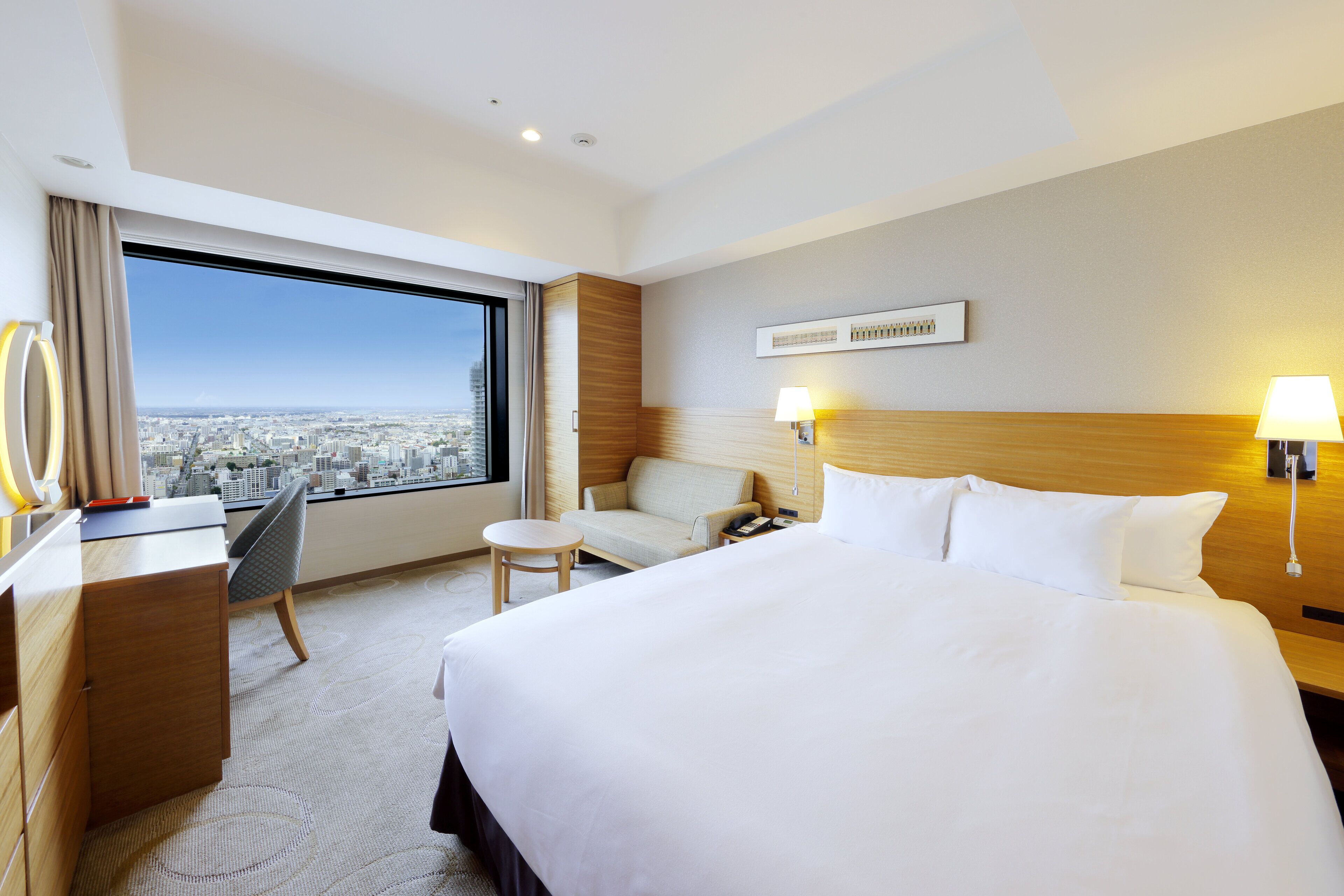 A hotel room with a large bed, a desk, a chair, and a view of the city.