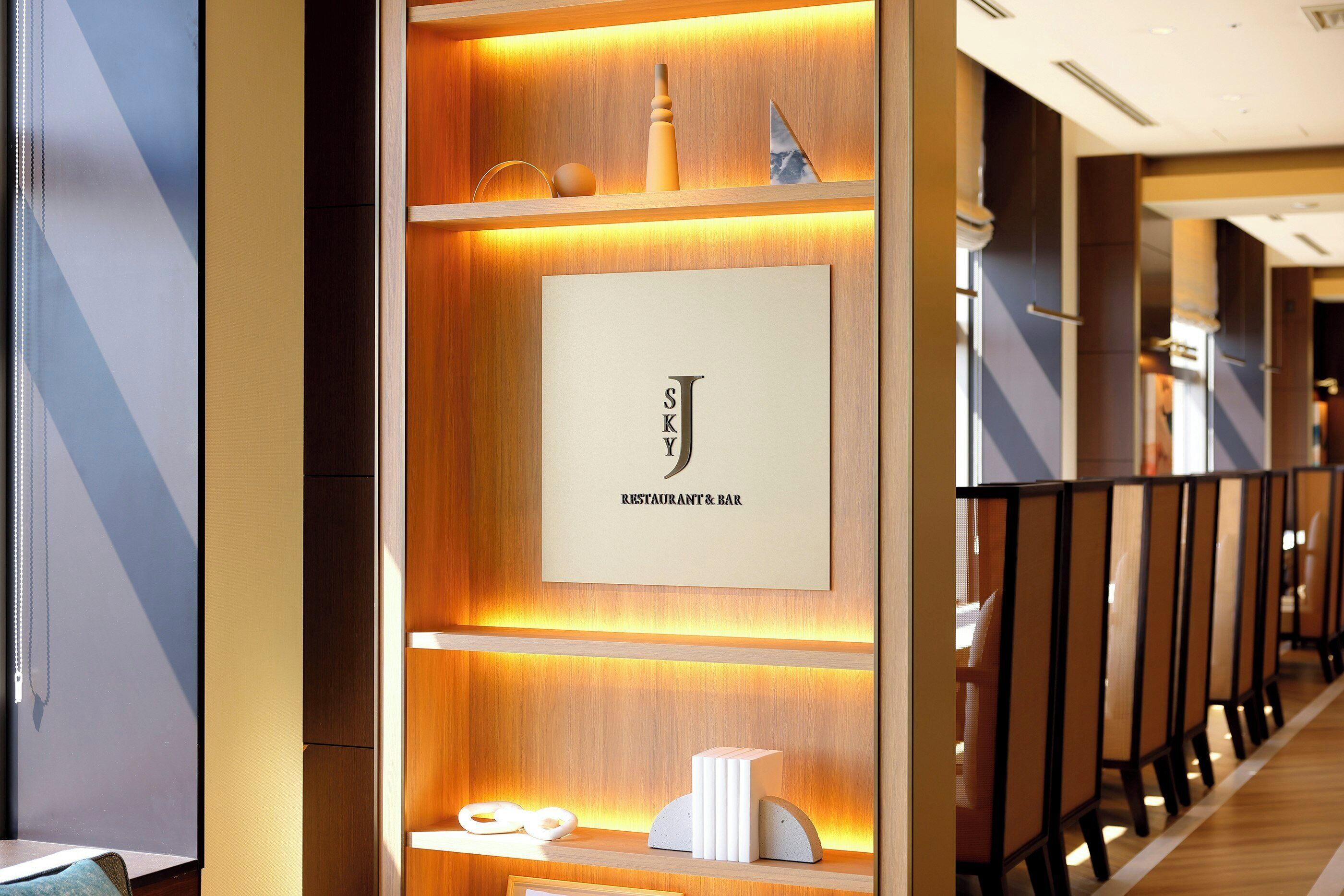 A modern interior with a wooden reception desk, a framed sign for a restaurant and bar, and a row of seating with partitions.