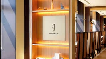 A modern interior with a wooden reception desk, a framed sign for a restaurant and bar, and a row of seating with partitions.