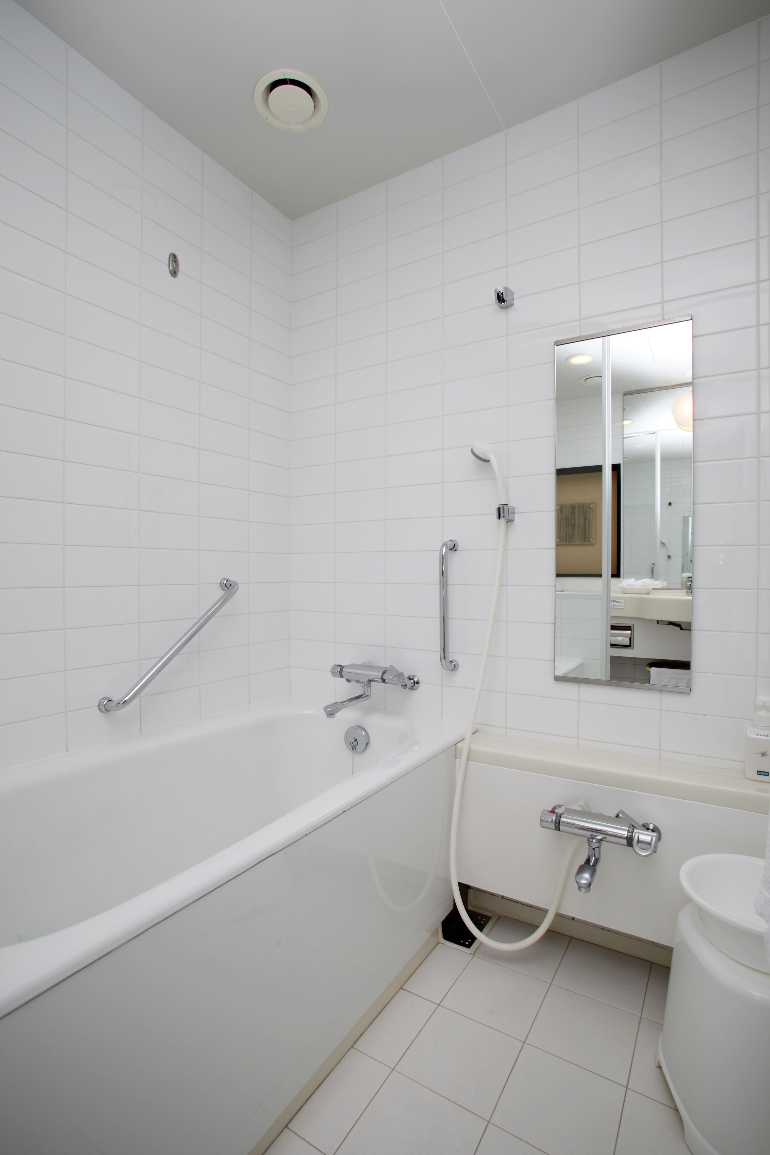 A modern bathroom with white tiles, a bathtub, a shower, a toilet, and a mirror.