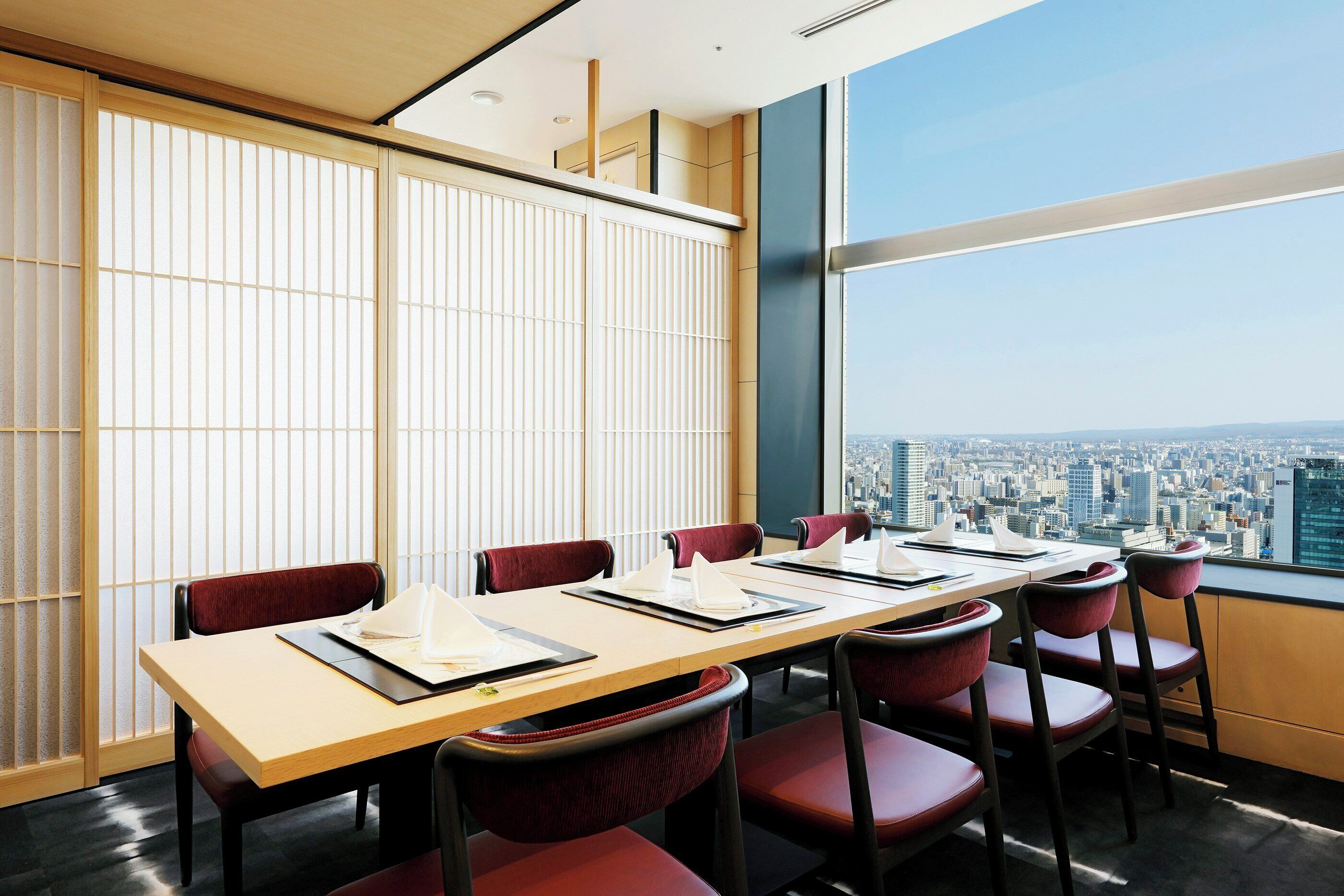 A conference room with a city view, wooden sliding doors, and red chairs.