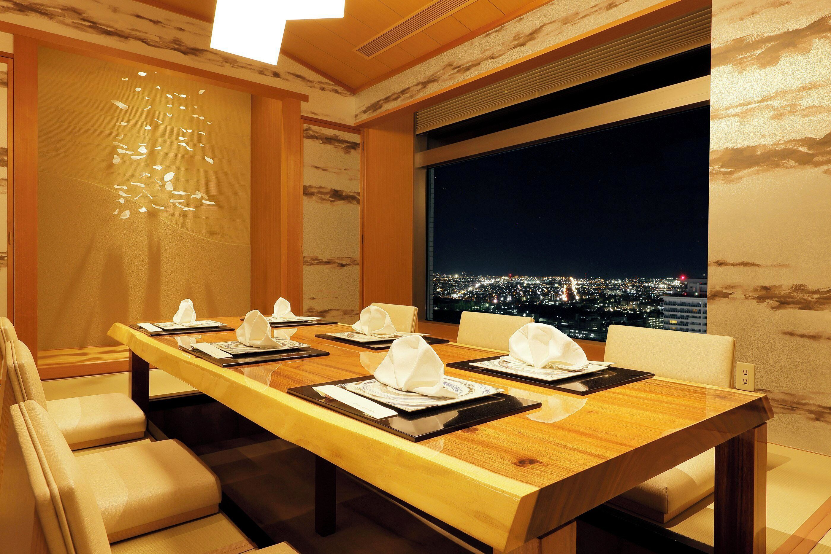 A conference room with a long table, chairs, and a cityscape view through a large window.