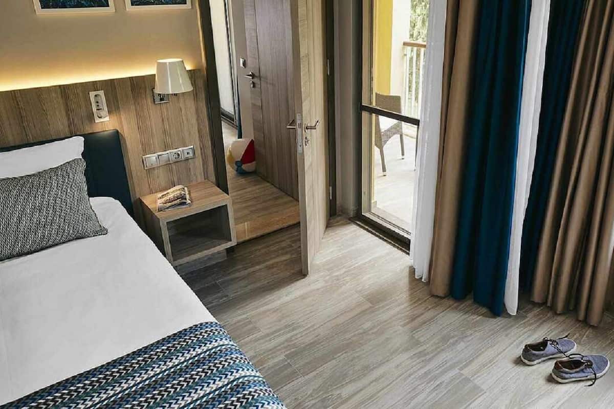 Ein Hotelzimmer mit Bett, Nachttisch, Lampe und Blick ins Freie durch eine Schiebetür.