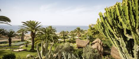 A lush garden with palm trees, a cactus, and a thatched-roof structure.