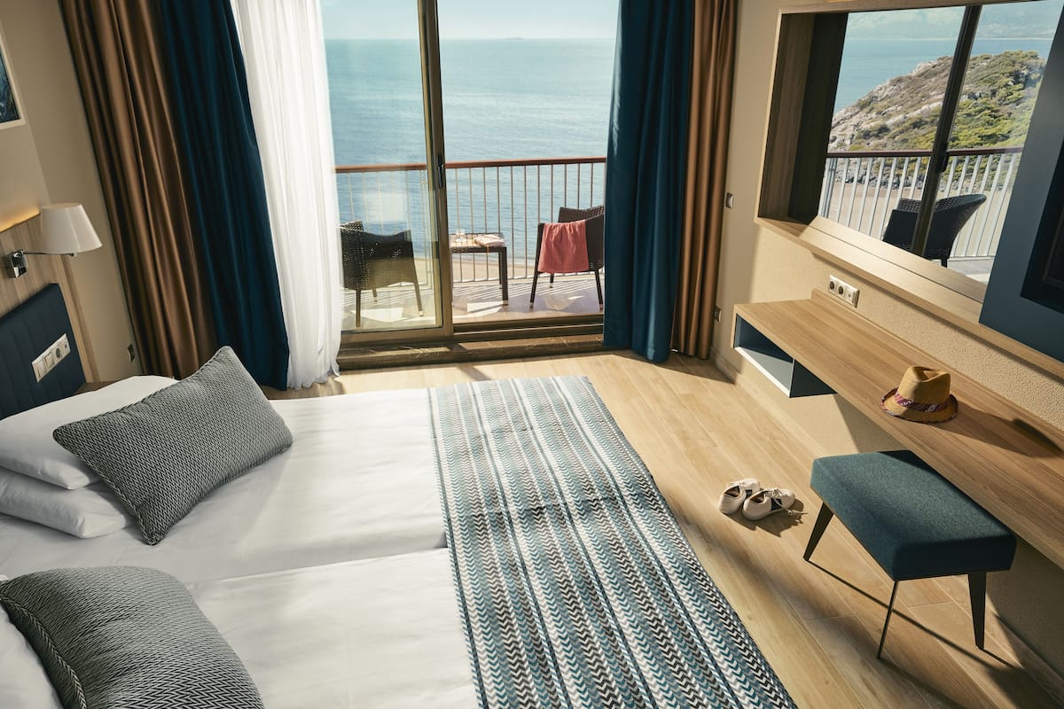 Ein Hotelzimmer mit einem großen Bett, einem kleinen Schreibtisch, einem Stuhl und Meerblick.
