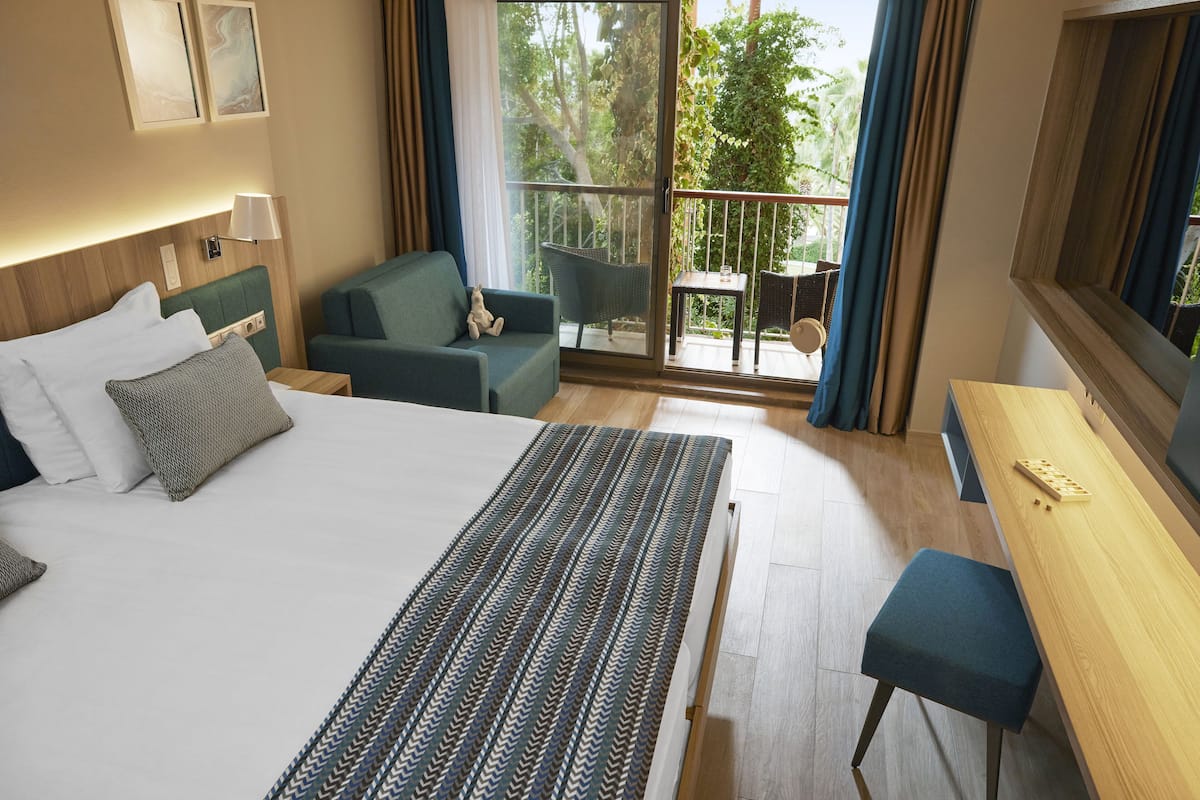 Ein Hotelzimmer mit einem großen Bett, einem Schreibtisch mit Stuhl, einer Couch und einem Balkon mit Tisch und Stühlen.