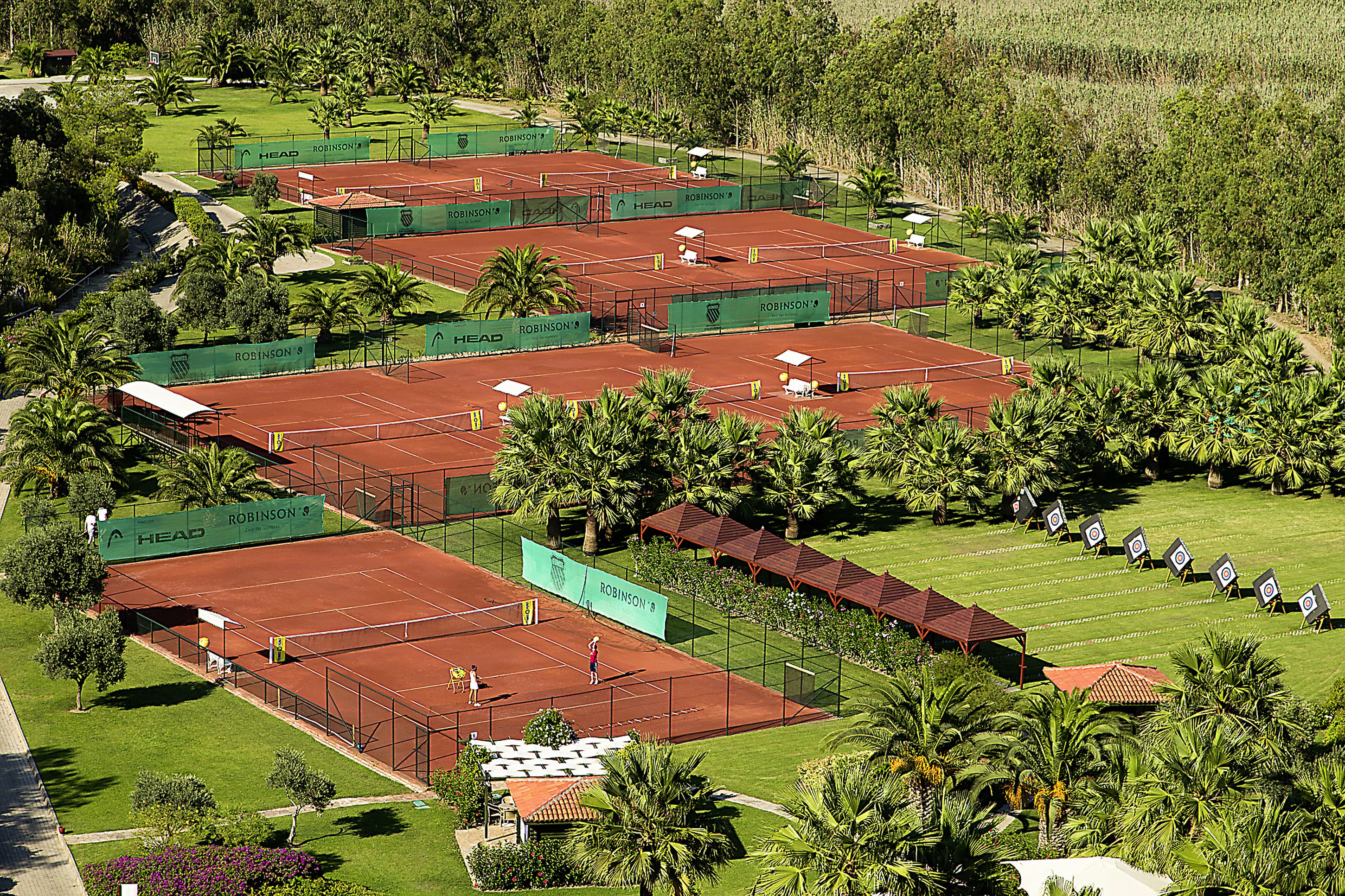 A tennis facility with multiple courts, surrounded by palm trees and greenery.