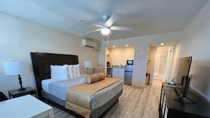 A hotel room with a bed, bedside tables, a desk, a chair, a ceiling fan, an air conditioning unit, a kitchenette, and a mirror. - Beachside Resort Motel (Treasure Island)