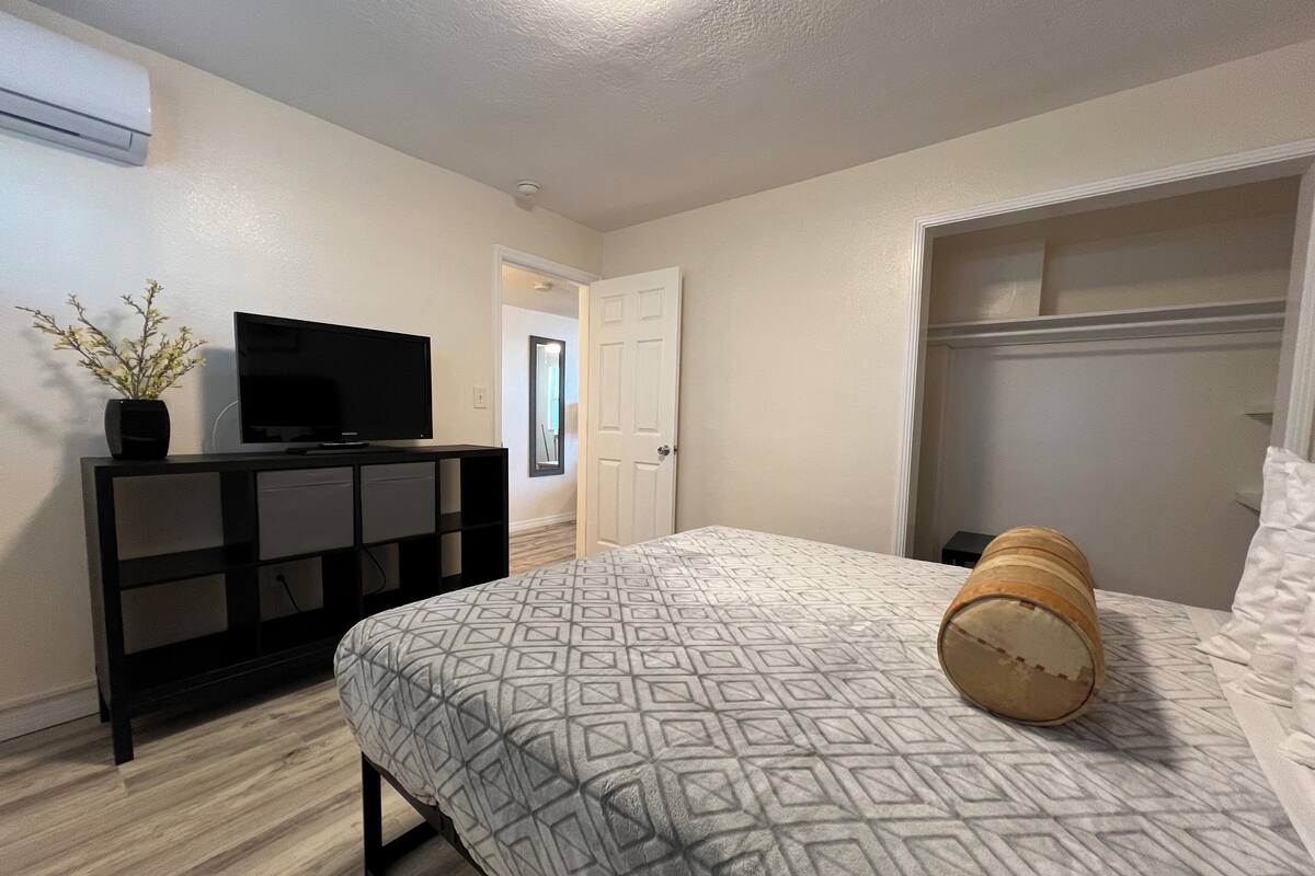 A bedroom with a bed, a TV on a black console, a wooden barrel, and a closet.