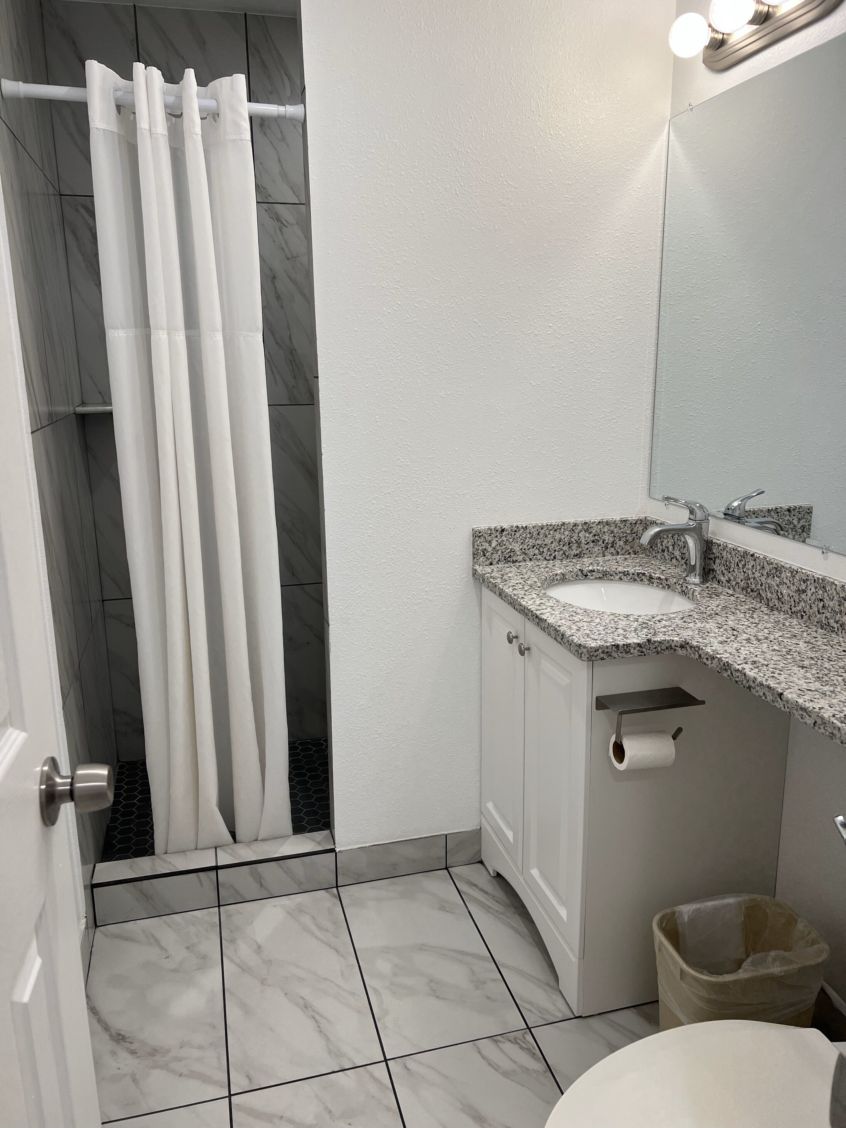 A bathroom with a shower curtain, a sink with a granite countertop, a mirror, and a toilet.