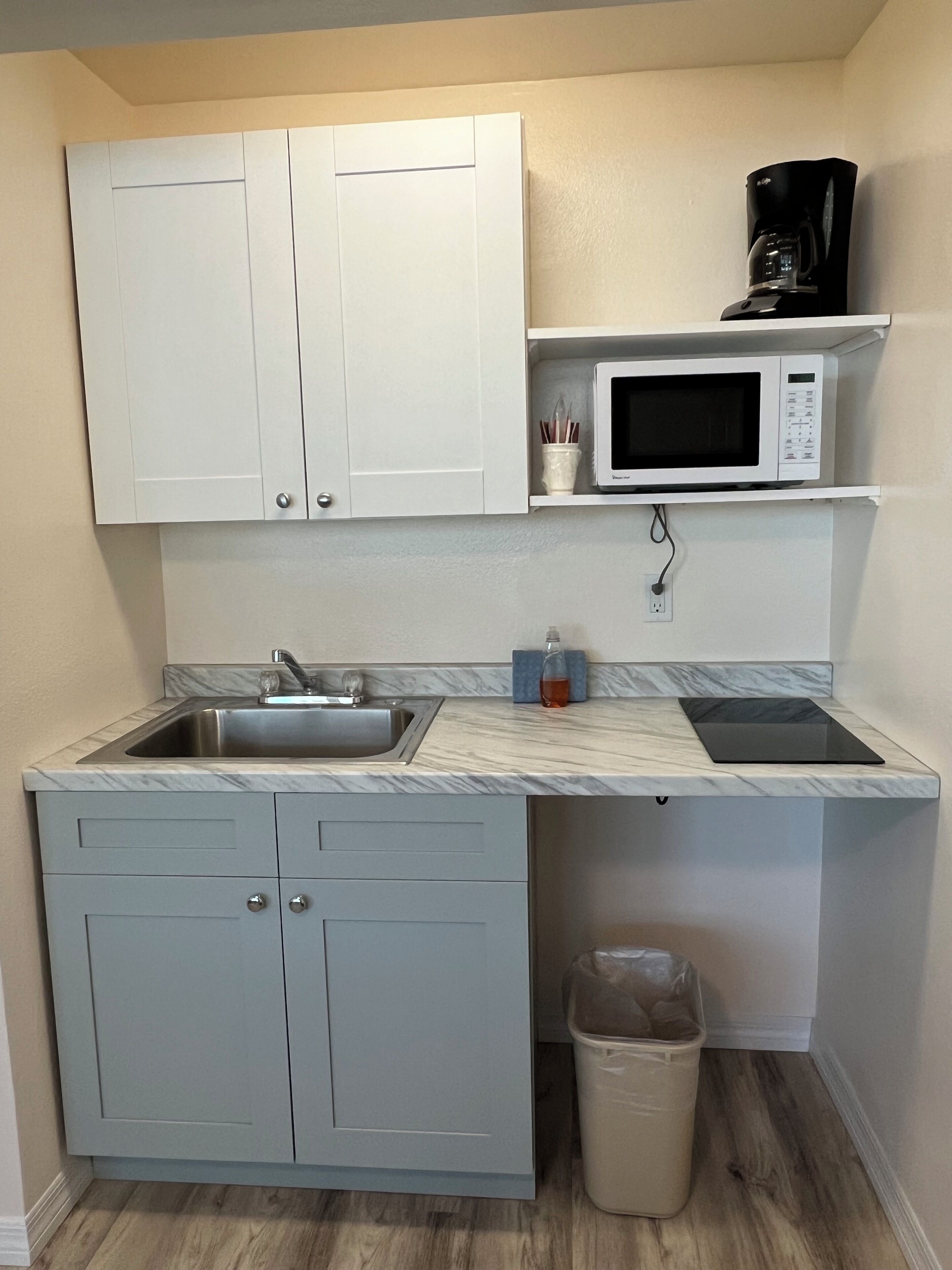 A compact kitchen with white cabinets, a sink, a microwave, and a coffee maker.