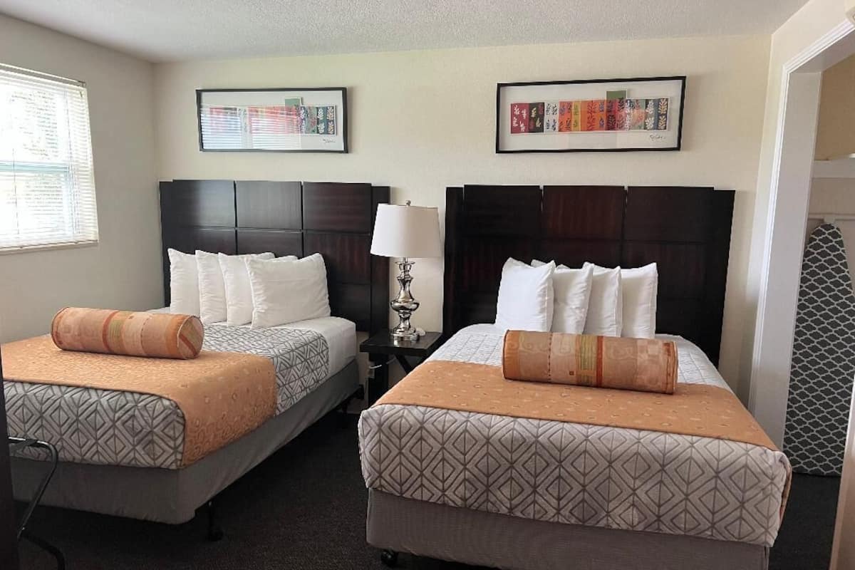 A hotel room with two beds, each with a patterned bedspread and pillows, a nightstand with a lamp, and framed artwork on the wall.
