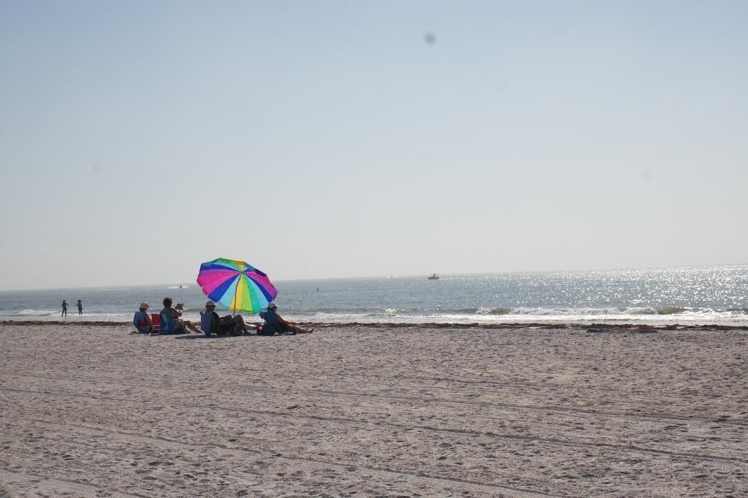 A beach with people sitting under a colorful umbrella.