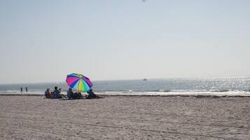 A beach with people sitting under a colorful umbrella.