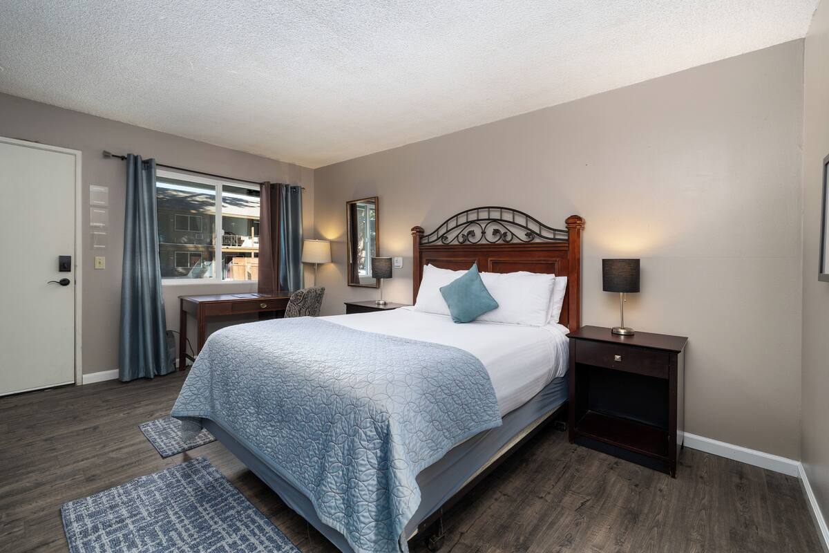 A bedroom with a large bed, a nightstand, a dresser, a window with curtains, and a door.