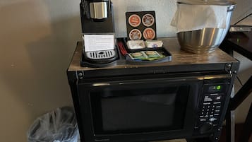 Una cocina compacta con cafetera, una bandeja de cápsulas de café y una olla sobre un microondas.