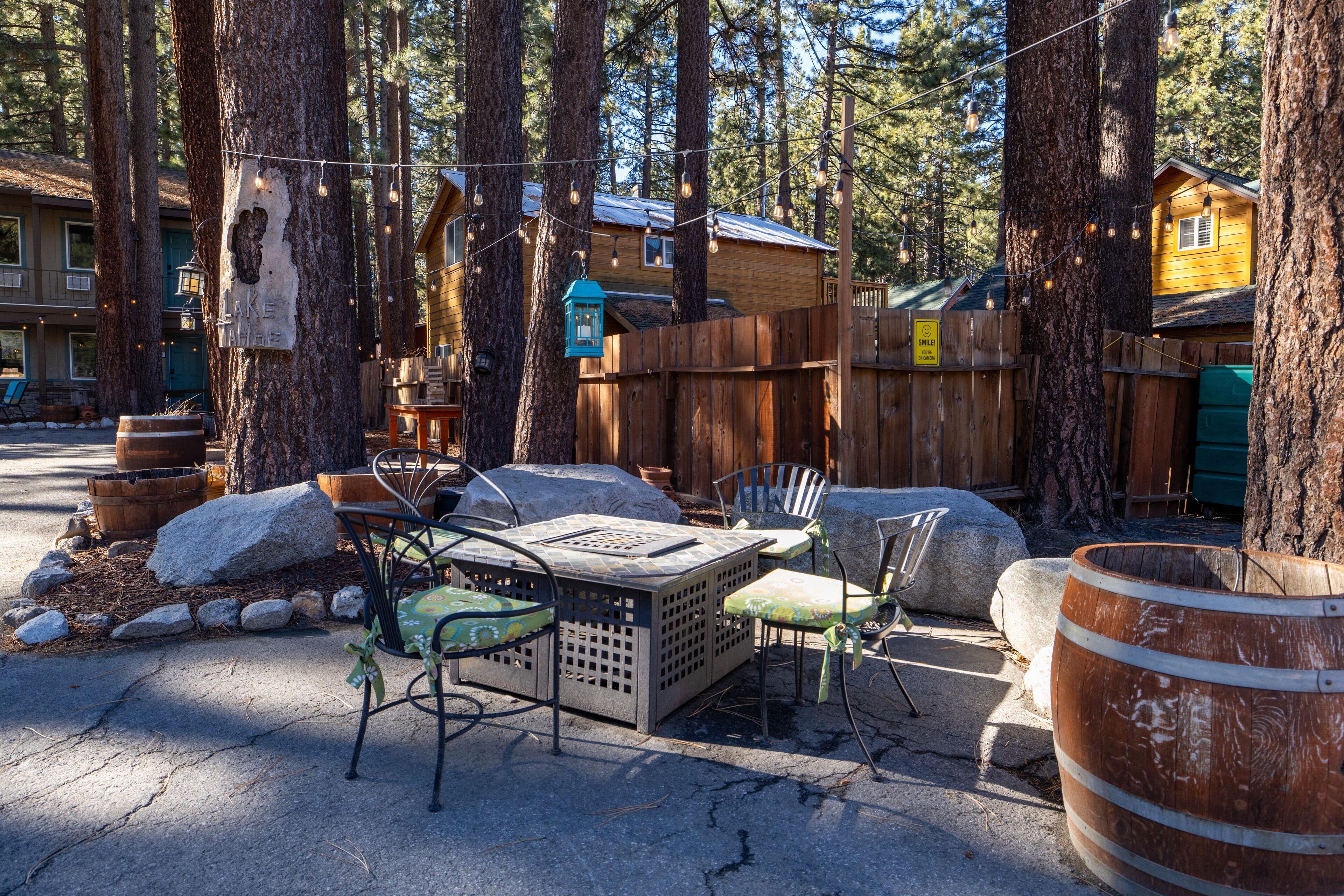Un espace extérieur aménagé dans un style rustique, avec une table et des chaises en bois, entouré de grands arbres et d’une clôture en bois.