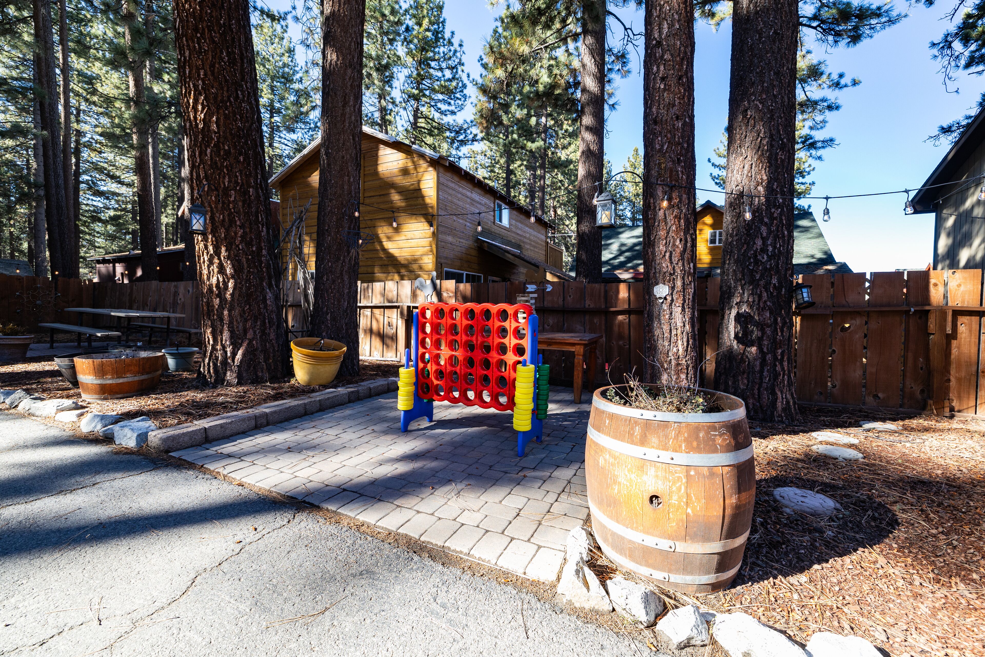 A wooden cabin with a deck, surrounded by tall trees, and a large barrel planter in the foreground.