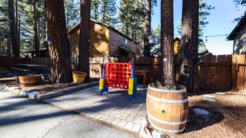 A wooden cabin with a deck, surrounded by tall trees, and a large barrel planter in the foreground.