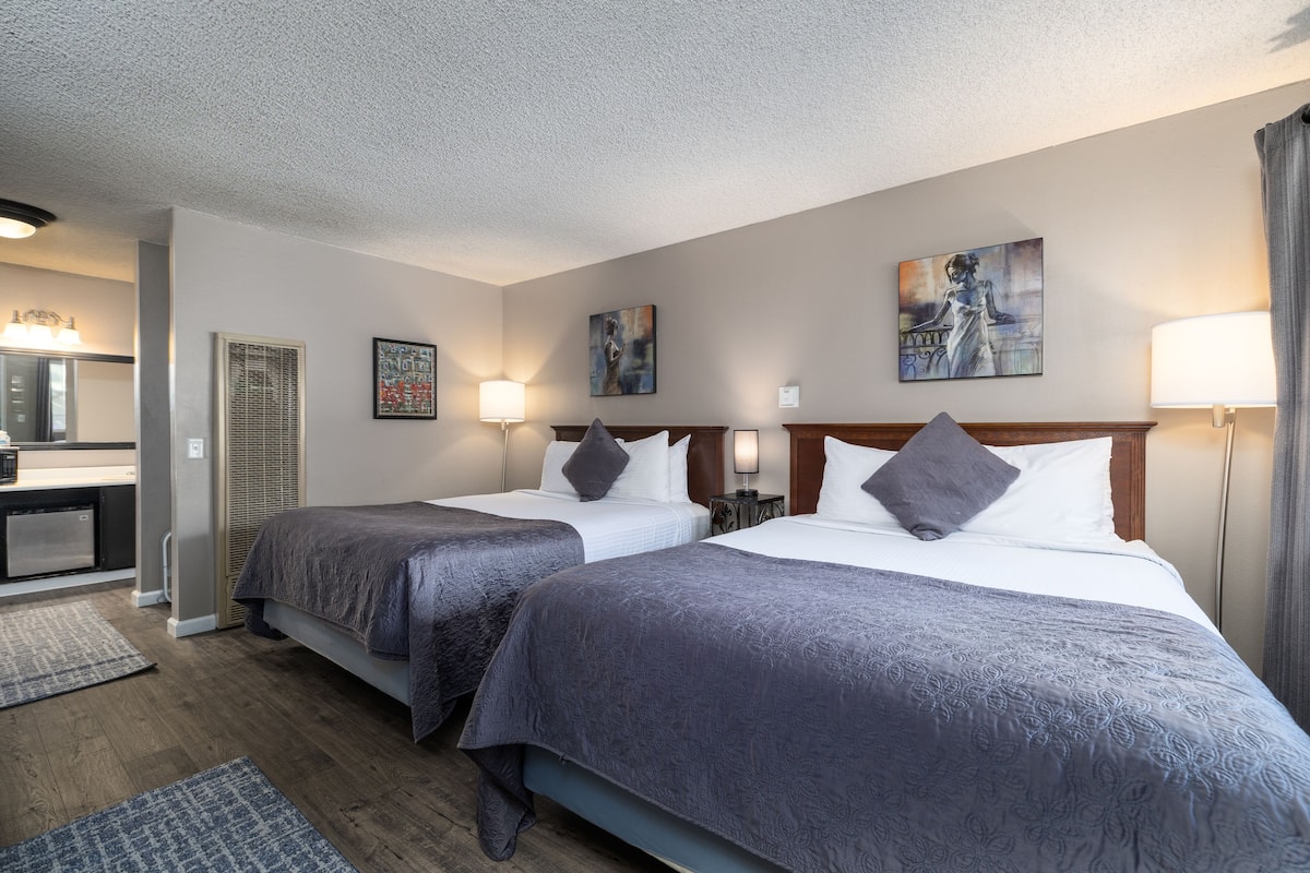 A hotel room with two beds, a desk, and a bathroom.