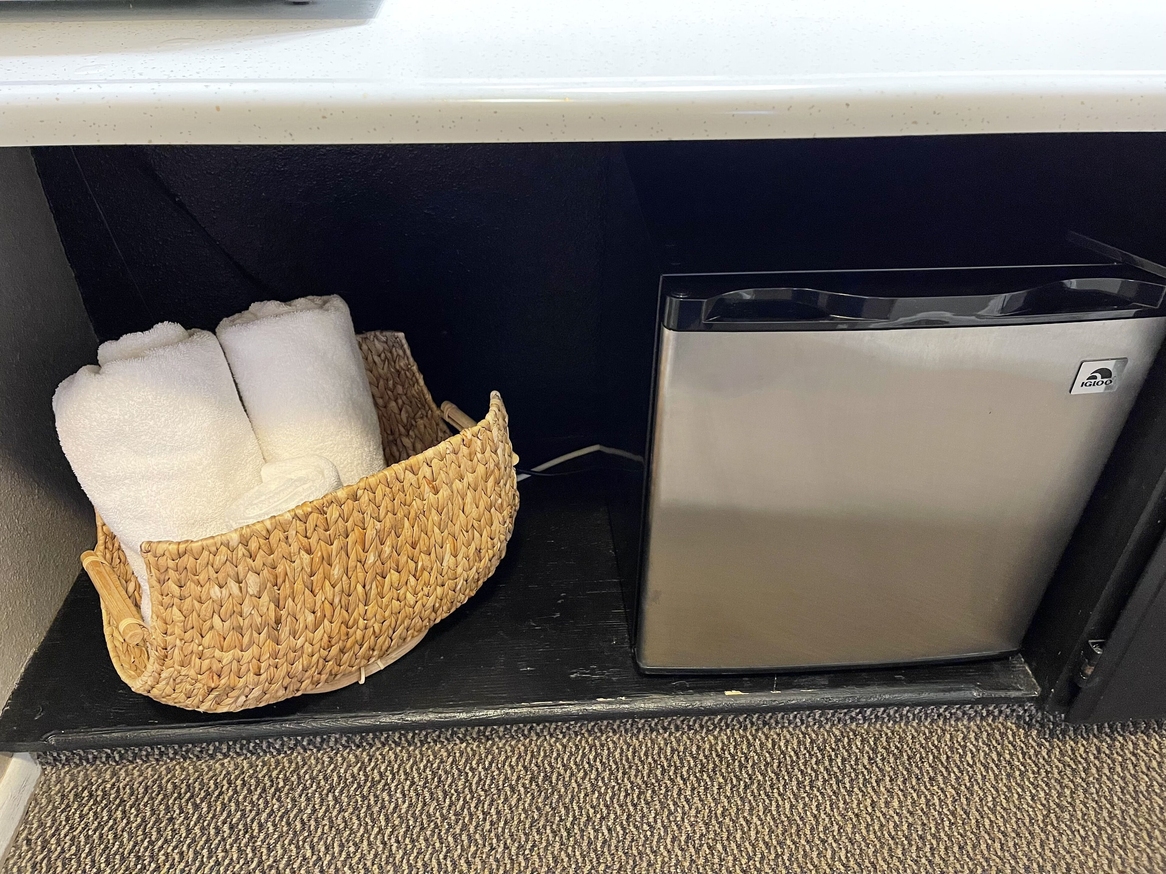 Un petit appareil métallique, peut-être une machine à café, est posé à côté d’un panier en osier contenant des serviettes pliées.