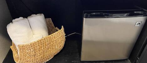 Un pequeño electrodoméstico metálico, posiblemente una cafetera, junto a una cesta tejida con toallas dobladas.