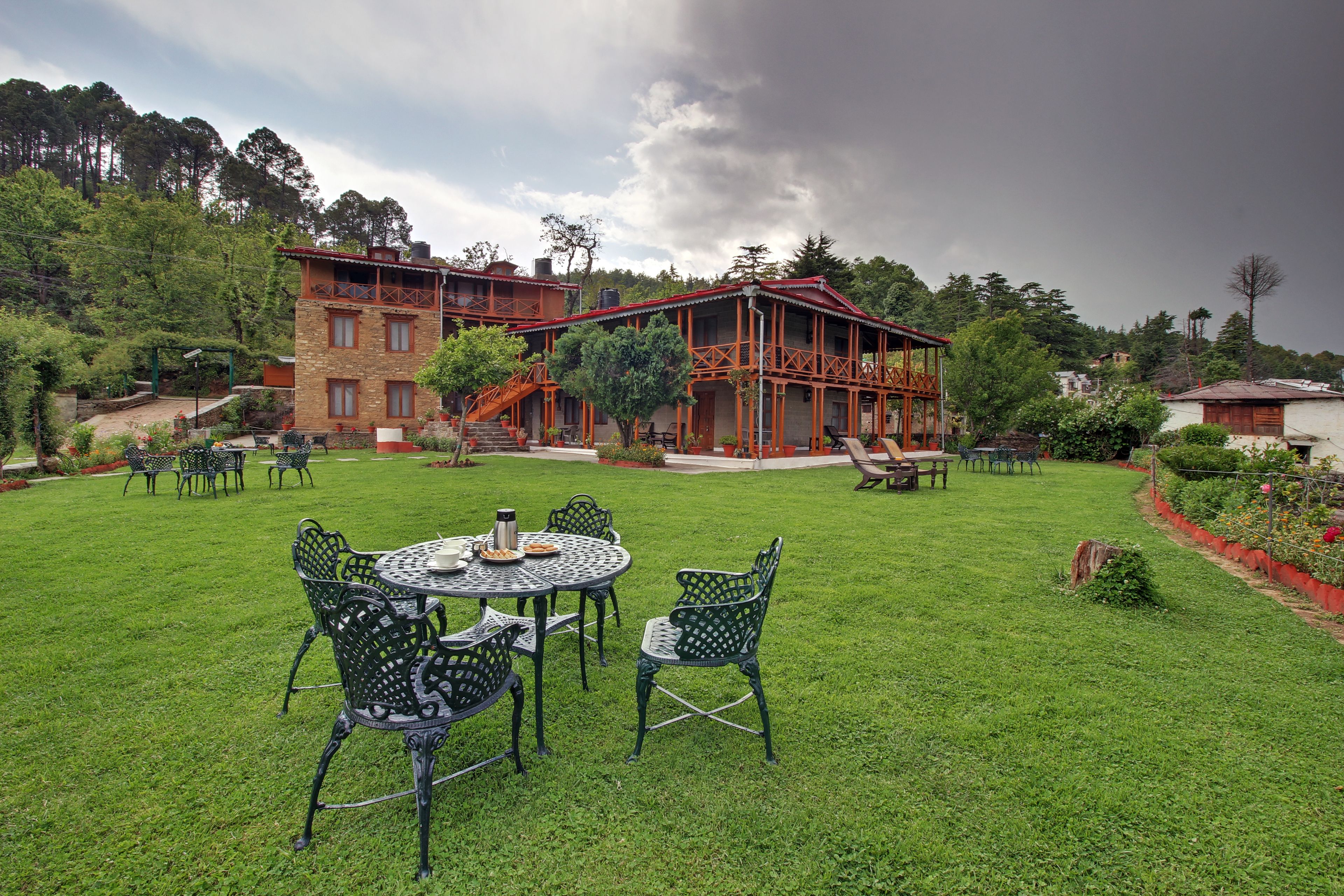 A spacious outdoor area with a dining set and chairs, a building with a red roof, and a garden with trees and plants.