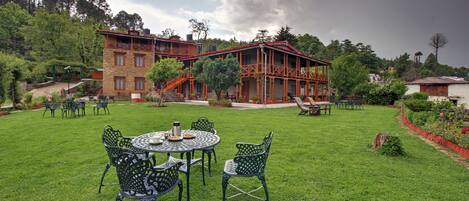 A spacious outdoor area with a dining set and chairs, a building with a red roof, and a garden with trees and plants.