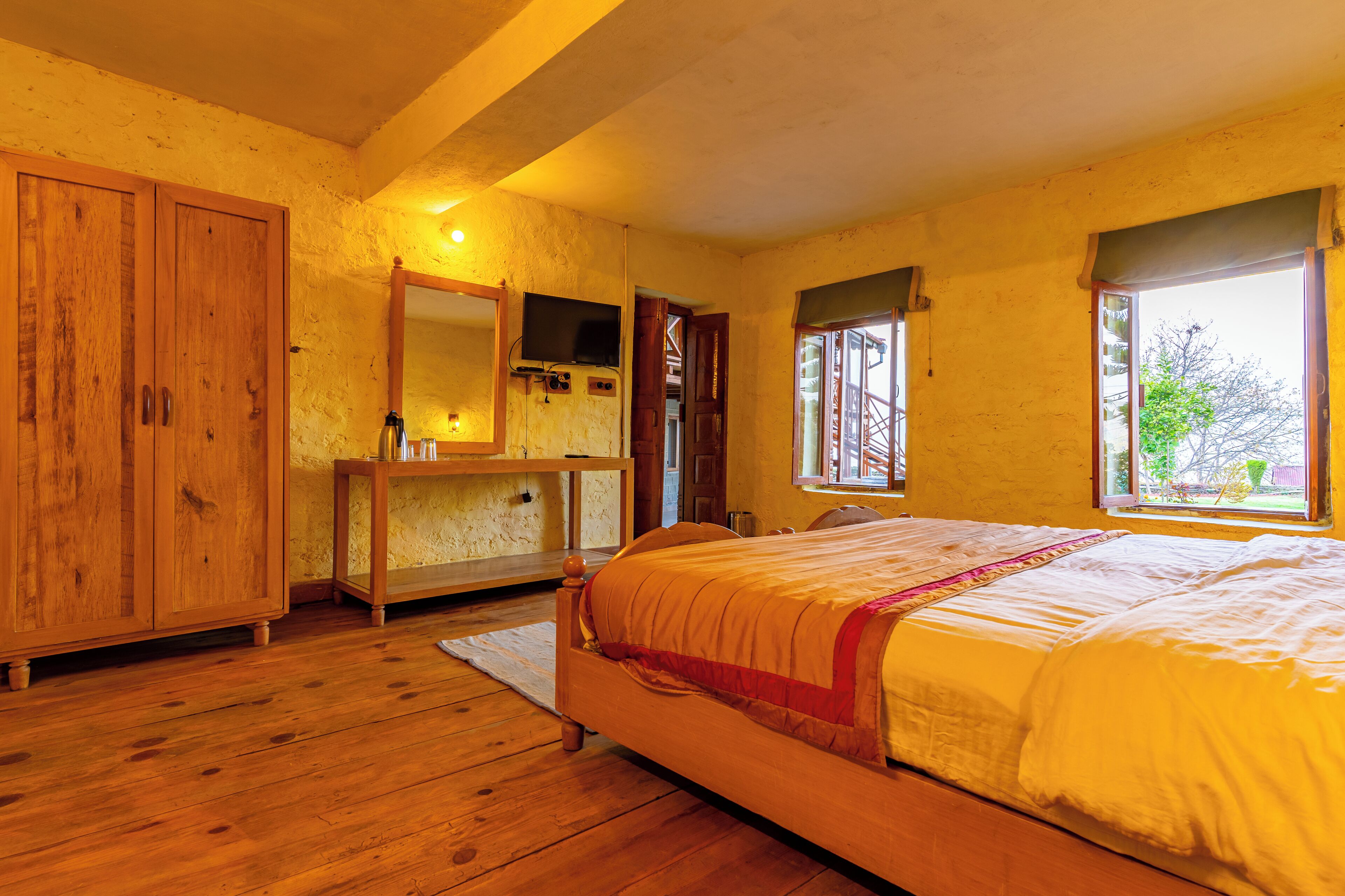 Een slaapkamer met een houten bed, een houten garderobe, een nachtkastje met spiegel, en een raam met uitzicht op groen.