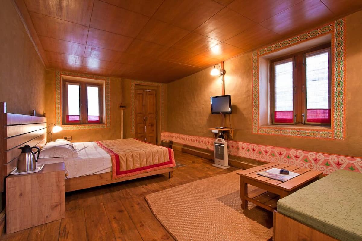 A cozy room with a wooden bed, a desk, a television, and a window with decorative trim.